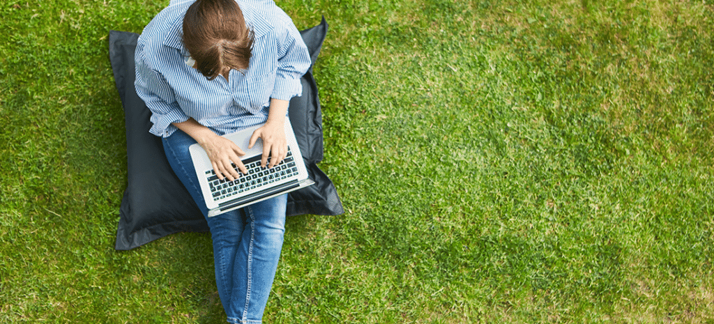 a woman works on a laptop outdoors in a large green space