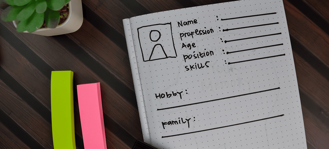 A designer sketches out a the specifics of a user persona at a wooden desk.