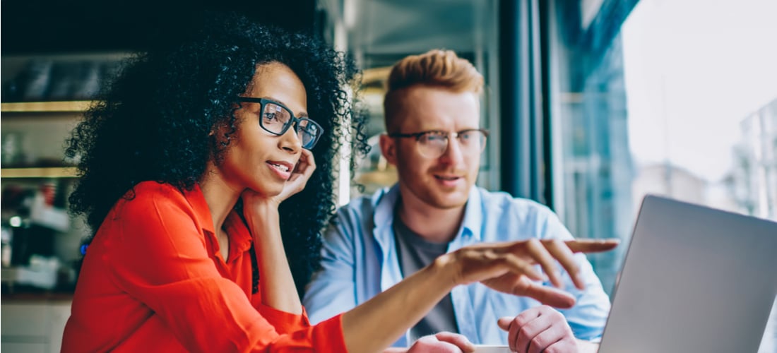 female graphic designer pointing with finger on laptop computer during collaboration with colleague