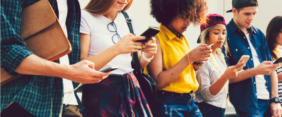 Photo of gen z'ers standing on a wall on their phones