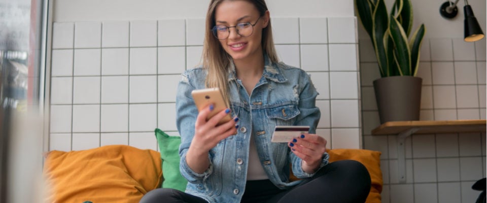 How to Create a WooCommerce Loyalty Program in WordPress. Photo of woman sitting comfortably using credit card to buy something on phone