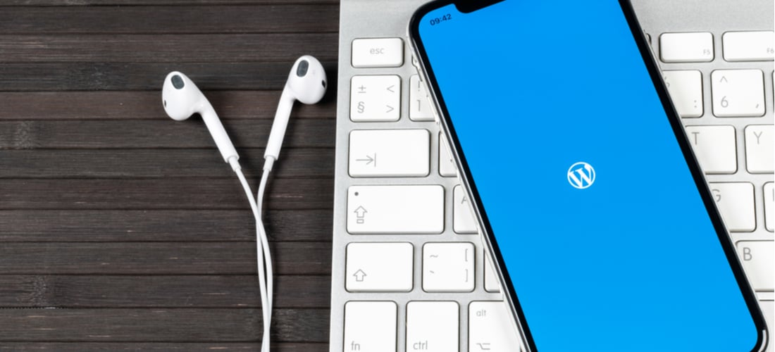 Picture of an Apple keyboard with headphone and a phone with WordPress logo pulled up