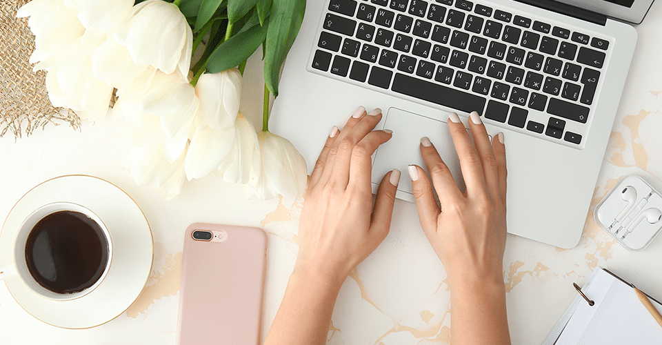 a woman works on a laptop at a desk next to flowers and a cup of coffee