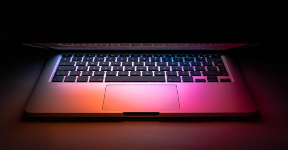 Image of Mac laptop in dark mode on desk with colorful light shining on keyboard. WordPress dark mode