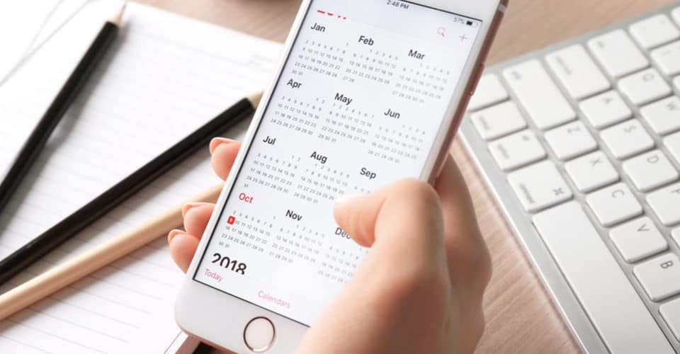 Person pressing phone calendar at desk with notebook and keyboard