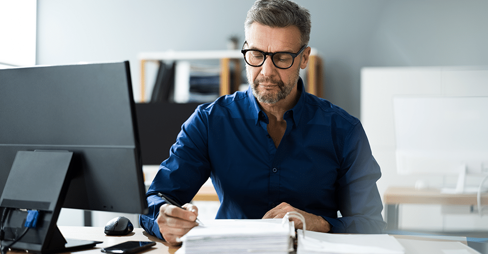 a businessman sits at a desk and looks over a stack of papers