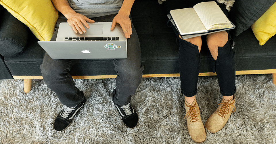 two developers discuss a website on a gray couch with yellow throw pillows