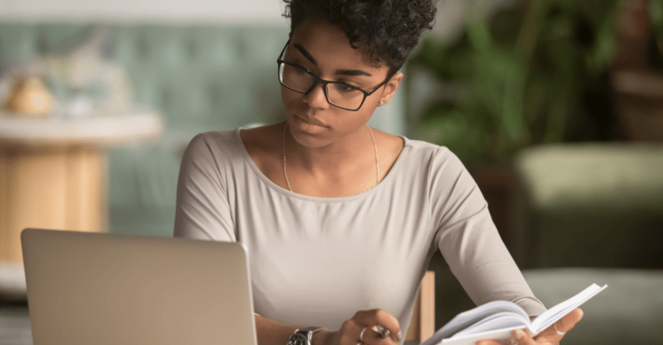 Woman sitting at desk learning WordPress looking at laptop and notebook