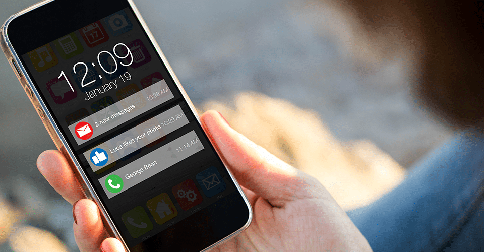 a person holds an iPhone showing the lock screen. The lock screen shows the time, the date, and three push notifications